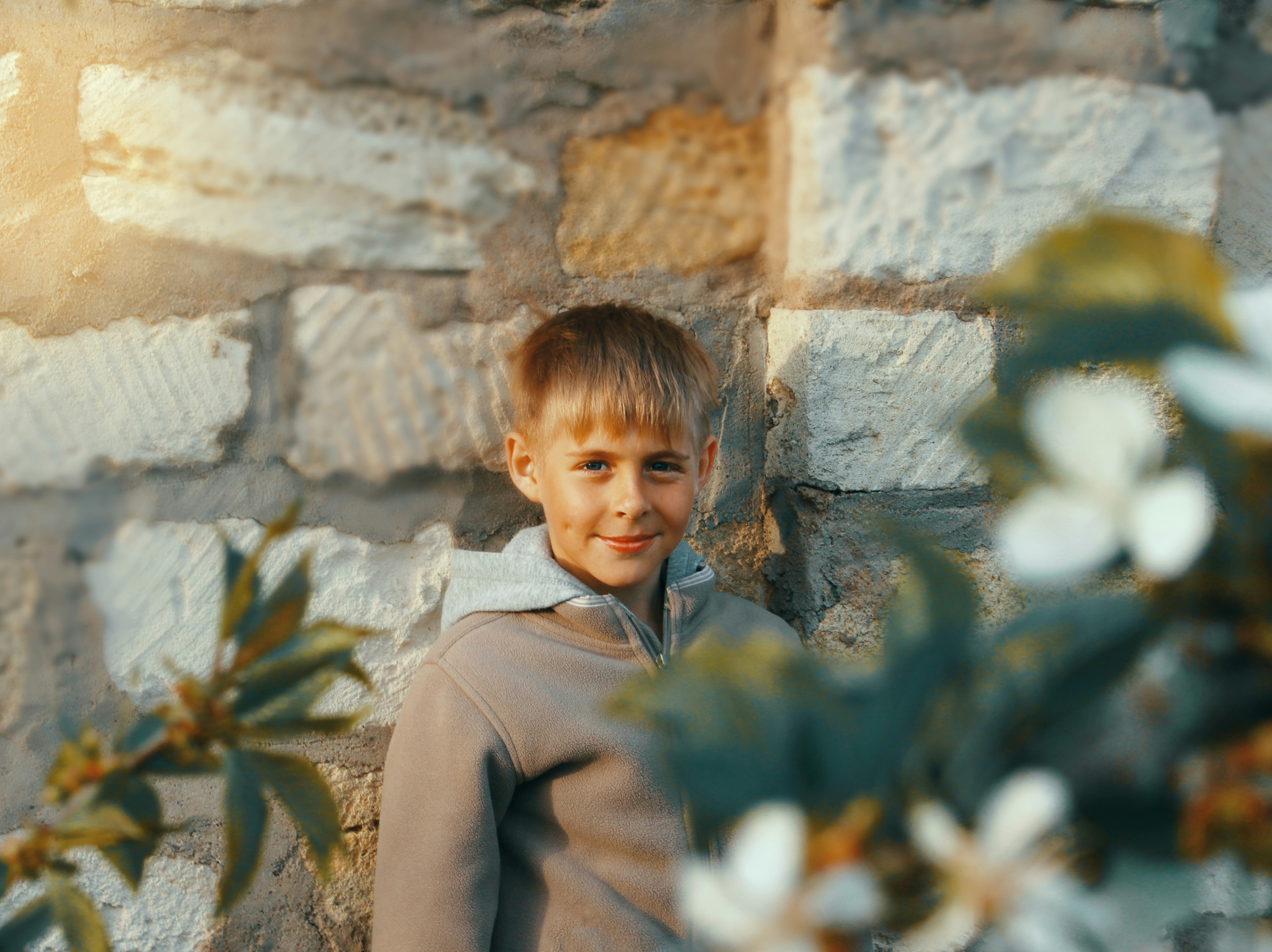 a young boy standing in front of a stone wall