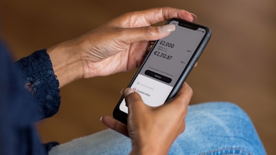 A person is holding a smartphone displaying a currency converter app. The screen shows conversion rates between GBP and EUR, with corresponding amounts.