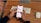 A person is holding a smartphone displaying a currency conversion app showing the exchange from GBP to DKK. The background contains a wooden desk with a keyboard and a computer mouse placed on it.