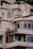 A section of a beige, multi-story building with large windows and balconies. The building has visible signs of wear and rust, particularly on the metal sign that appears to be corroded. Some air conditioning units are mounted on the walls, and the roof features various equipment and structures.