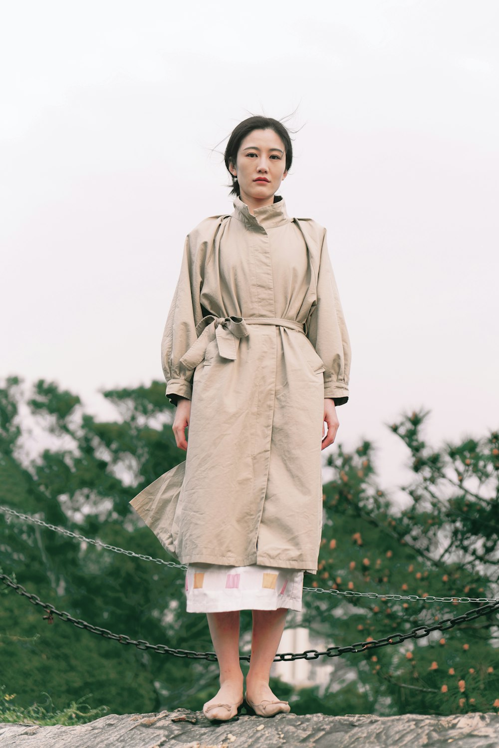 a woman in a trench coat standing on a rock