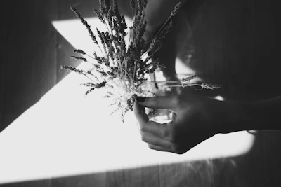 Softly lit close-up of hands holding a blooming wildflower bouquet against a cream background.