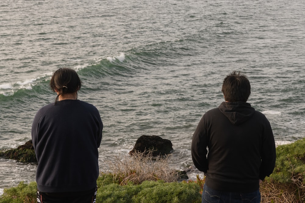 a couple of men standing on top of a cliff next to the ocean