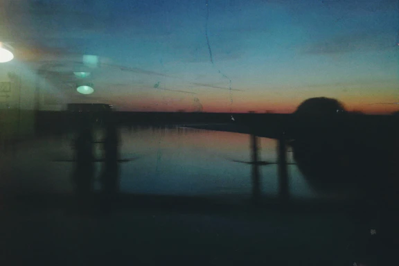 A sleek, modern glass panel with soft shadows showcasing a serene sunset over a calm ocean, reflecting the luxurious and tranquil vibe of vialuxe.