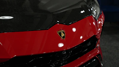 Close-up of a sleek sports car hood glistening with starcolor's racing red automotive paint under bright lights.