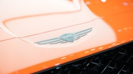 Close-up of a Genesis emblem on a polished hood, reflecting a pristine city skyline.