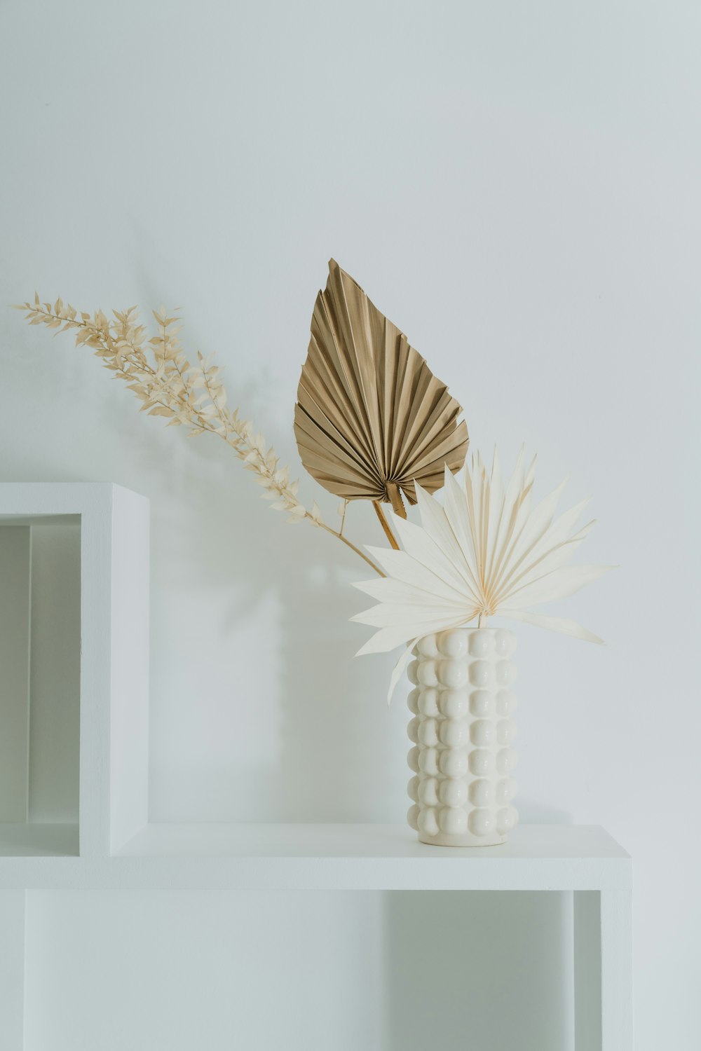 a white shelf with a vase and a plant