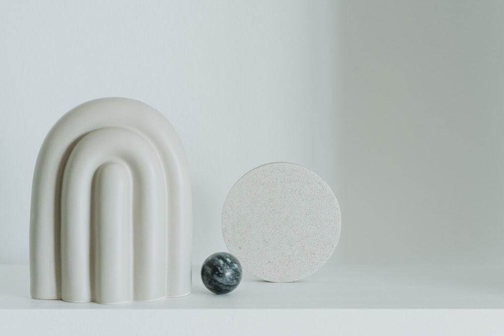 a white sculpture with a marble ball next to it