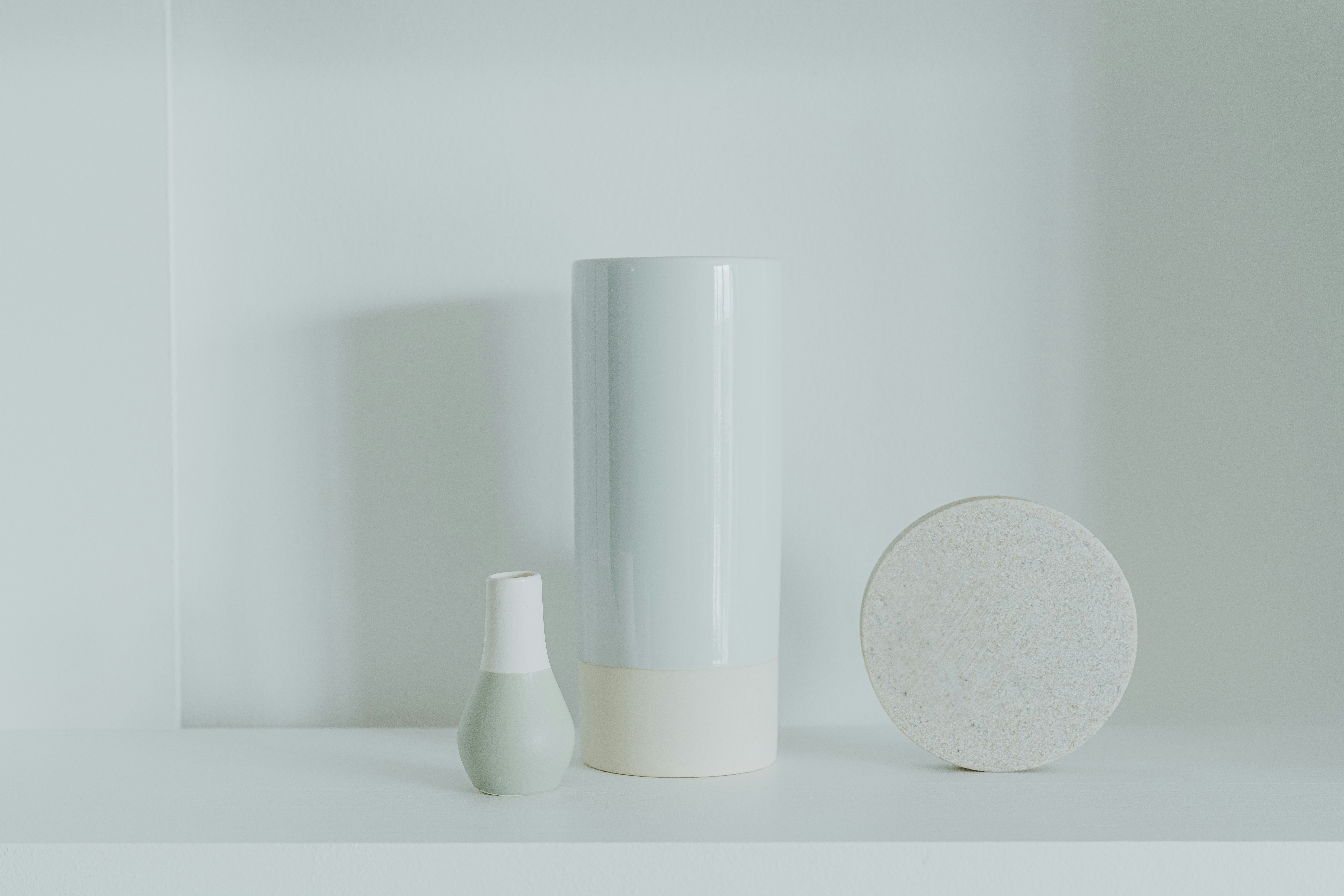 a white vase sitting next to a white vase on a shelf
