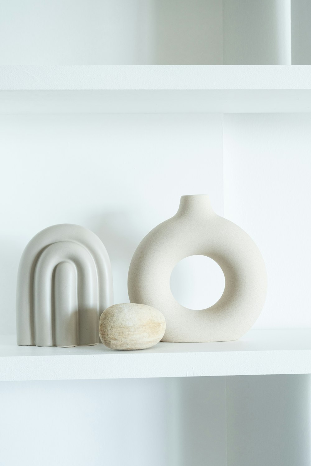 a white shelf with a white vase and a white object on it