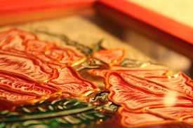 Close-up view of an embossed glass art piece featuring detailed red rose petals with golden outlines. The composition includes green leaves, adding contrast against the warm tones of the petals. The artwork is framed in a rectangular shape.