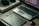 A workspace featuring a laptop with photo-editing software open, a graphics tablet, a digital pen in a holder, and a box labeled 'Wacom Intuos Pro.' Additionally, there's a DSLR camera resting on the box.