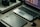 A workspace featuring a laptop with photo-editing software open, a graphics tablet, a digital pen in a holder, and a box labeled 'Wacom Intuos Pro.' Additionally, there's a DSLR camera resting on the box.