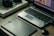 A workspace featuring a laptop with photo-editing software open, a graphics tablet, a digital pen in a holder, and a box labeled 'Wacom Intuos Pro.' Additionally, there's a DSLR camera resting on the box.