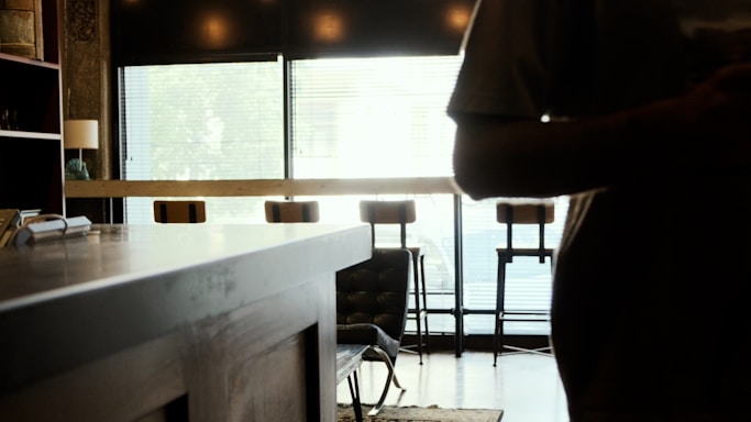 A dimly lit bar interior with empty stools and a polished wooden counter, hinting at a quiet Tokyo night.