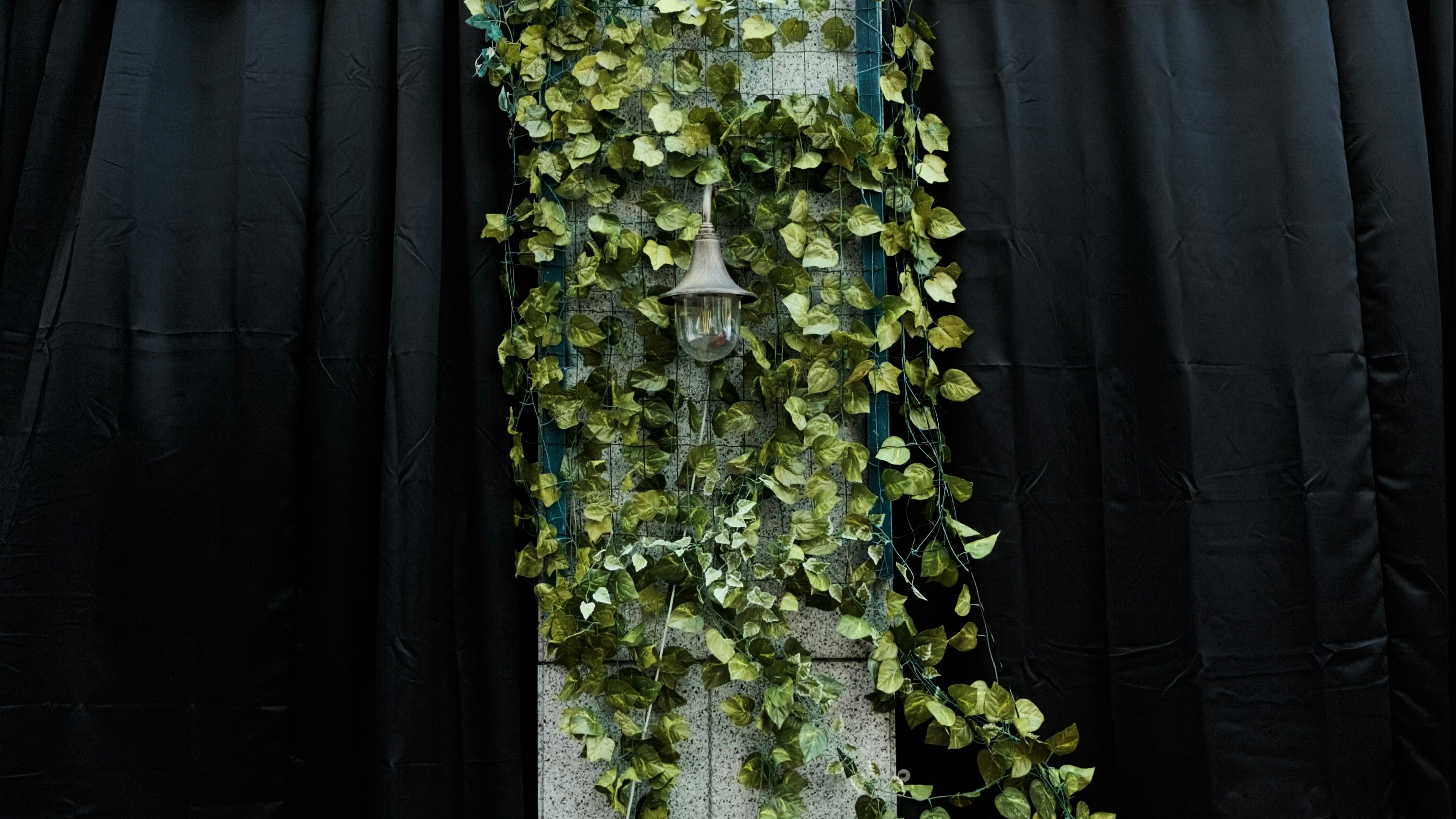 a white clock covered in green leaves next to a black curtain