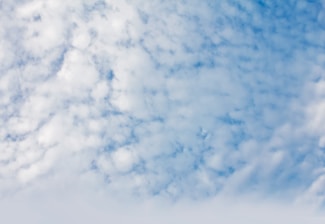 A sky filled with scattered, fluffy white clouds against a blue backdrop. The clouds appear soft and spread across the upper part of the image, providing a serene and airy atmosphere.