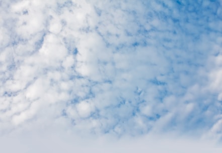 A sky filled with scattered, fluffy white clouds against a blue backdrop. The clouds appear soft and spread across the upper part of the image, providing a serene and airy atmosphere.