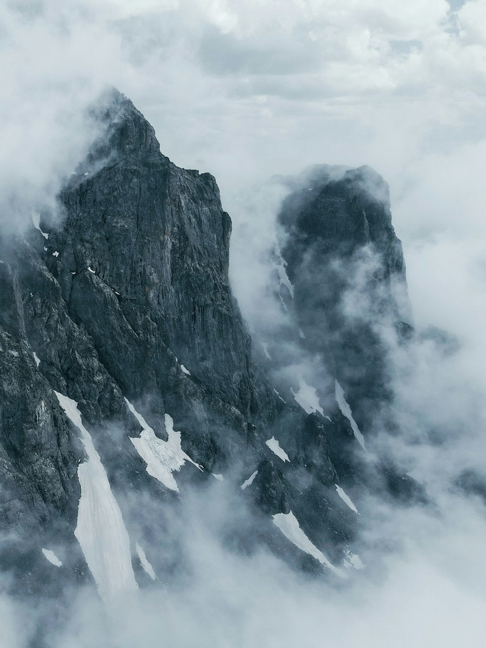 a mountain covered in snow and clouds under a cloudy sky