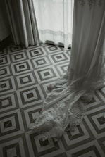 A wedding dress carefully covered and hanging in a softly lit room.