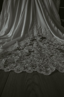 A detailed view of an elegant fabric with intricate floral lace patterns. The fabric drapes gracefully, showcasing its delicate design and texture on a flat wooden surface.