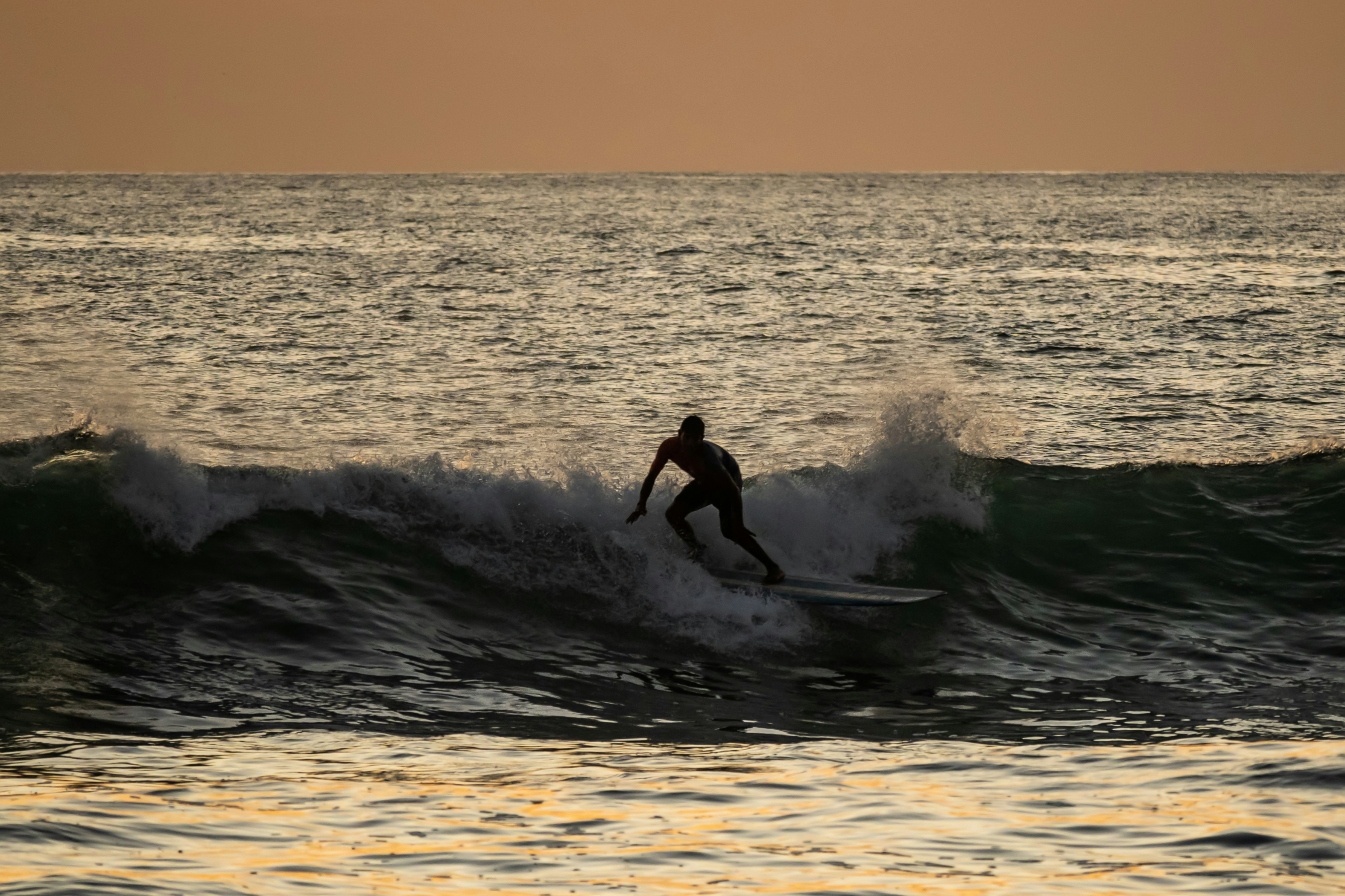 Sunset Surfing in Nosara - This stunning photograph captures the exhilarating thrill of surfing in the warm waters of Nosara, Costa Rica. The silhouette of the surfer is set against the golden hues of a magnificent sunset, as he rides the waves with incredible skill and grace. The natural beauty of the coastline, combined with the excitement of the sport, makes for an unforgettable experience. This photograph perfectly captures the sense of adventure and joy that surfing in Nosara offers.