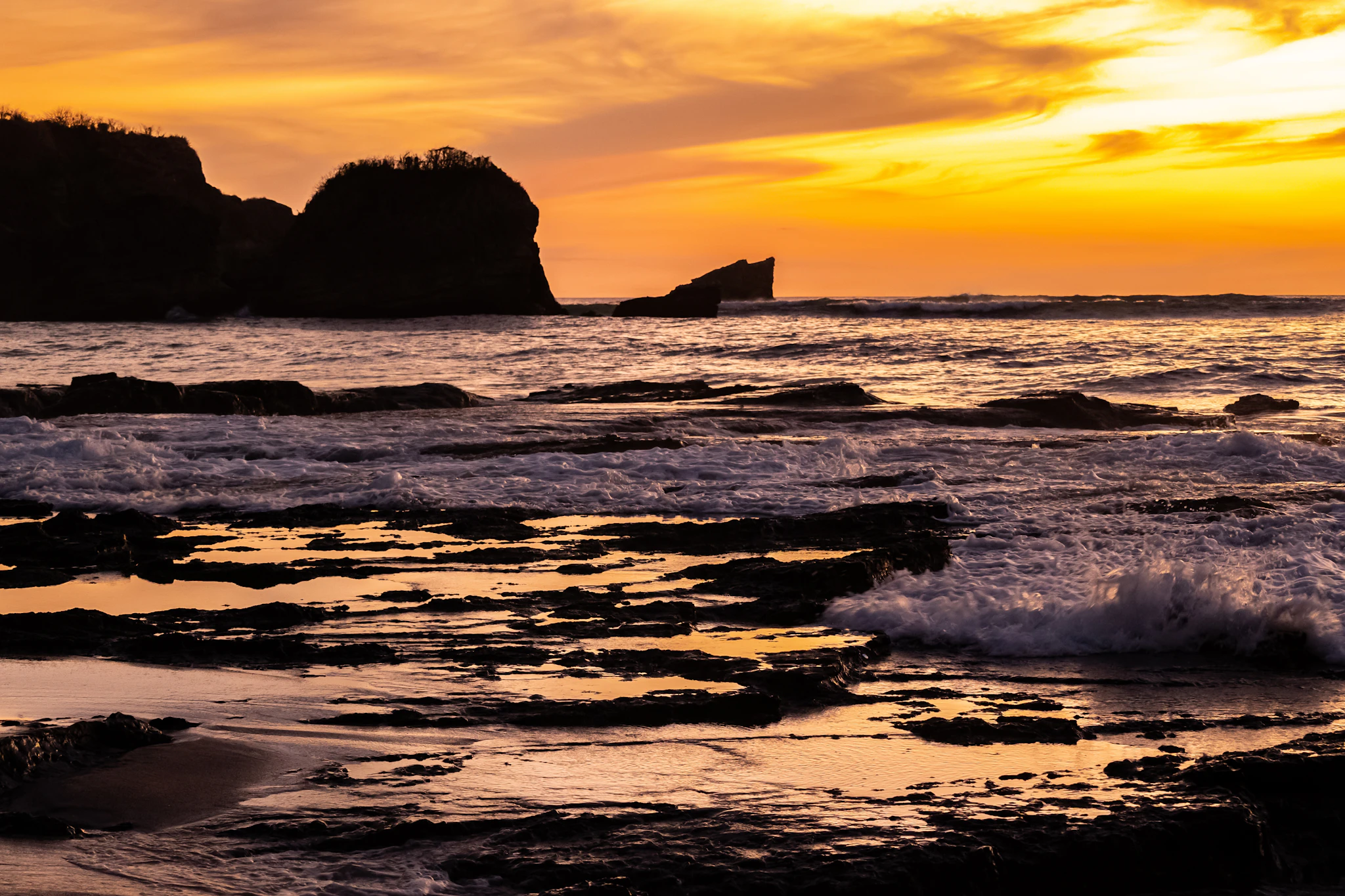 Sunset over the Pacific at Nosara, Costa Rica, waves breaking on the rocks