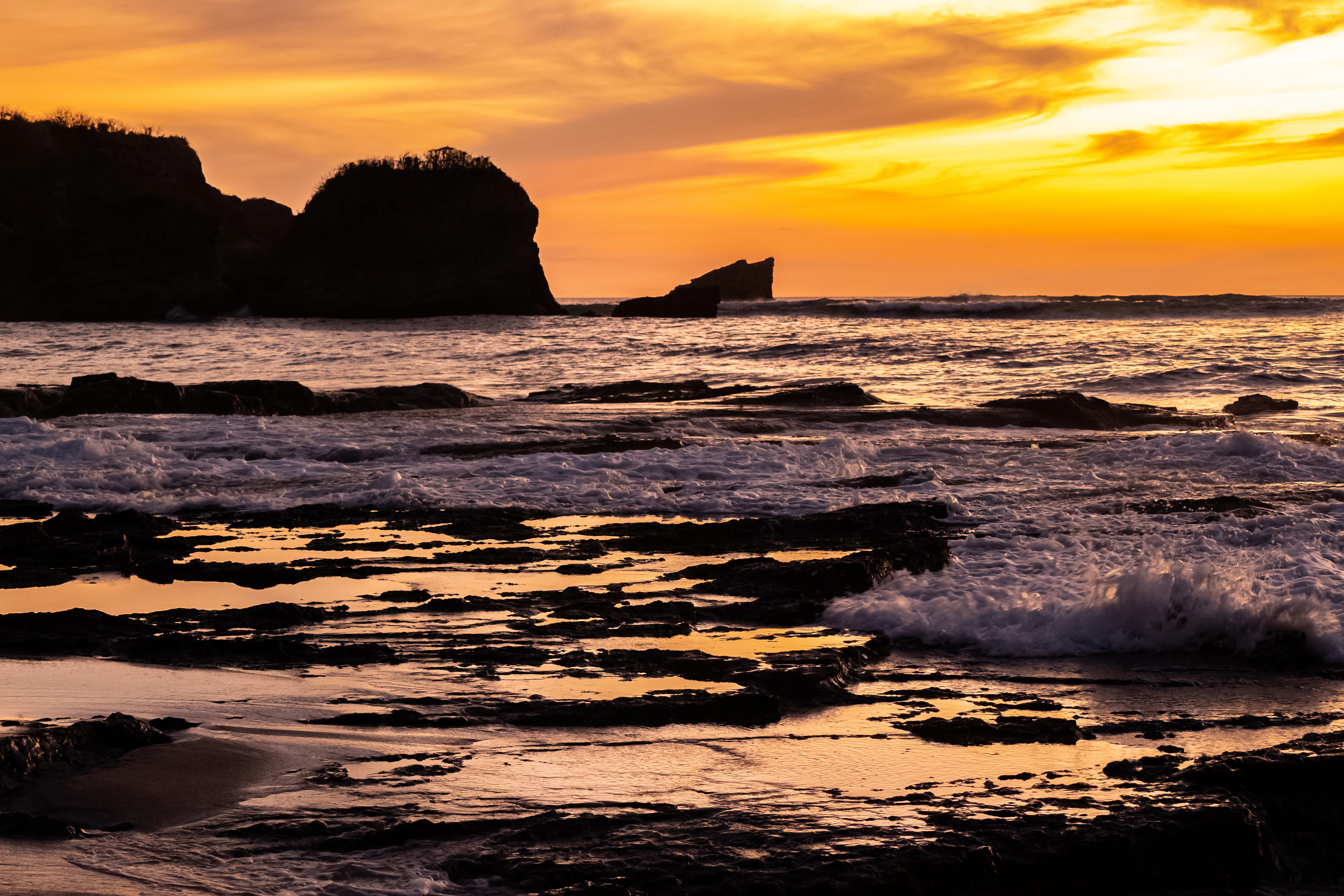 Sunset over the Pacific at Nosara, Costa Rica, waves breaking on the rocks