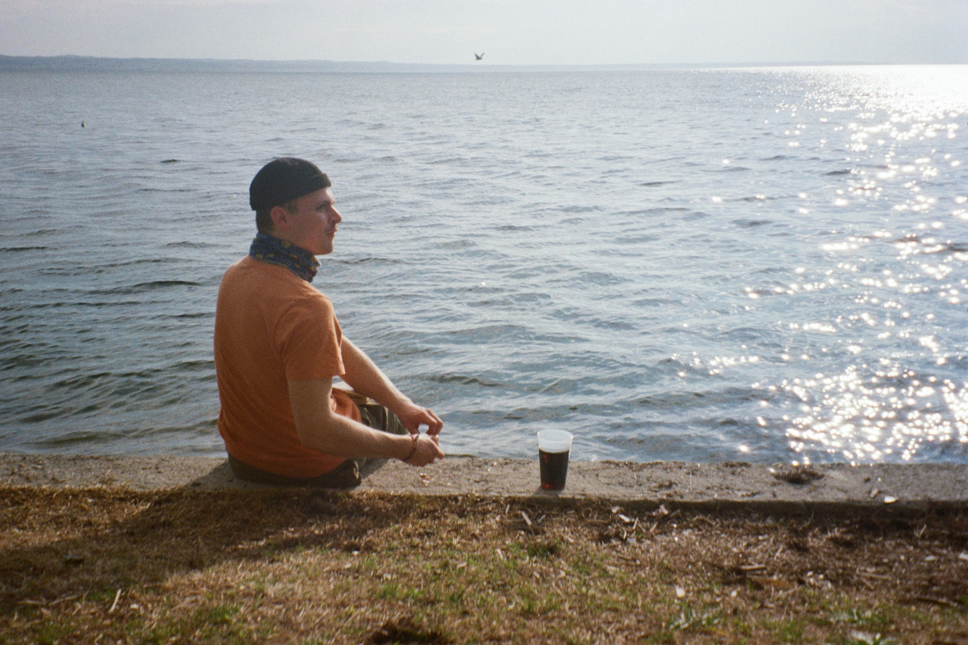 a man sitting on the edge of a cliff next to a body of water