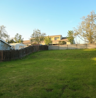 a grassy yard with a fence and a house in the background