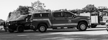 A black and white image featuring multiple emergency response vehicles, including a fire truck marked 'Waco Fire Battalion Chief' and another vehicle labeled 'Elm Mott'. The scene is outdoors with trees in the background and the vehicles are parked on a gravel surface.
