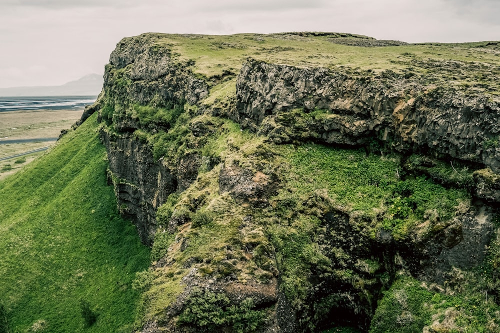 a rocky cliff covered in green grass next to a body of water