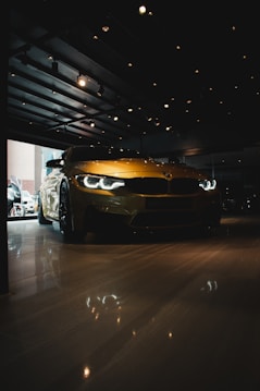 A sleek, yellow sports car is parked inside a dimly lit showroom. The car's headlights are illuminated, reflecting on the polished floor. Ceiling lights add a warm glow, creating a luxurious and sophisticated ambiance.
