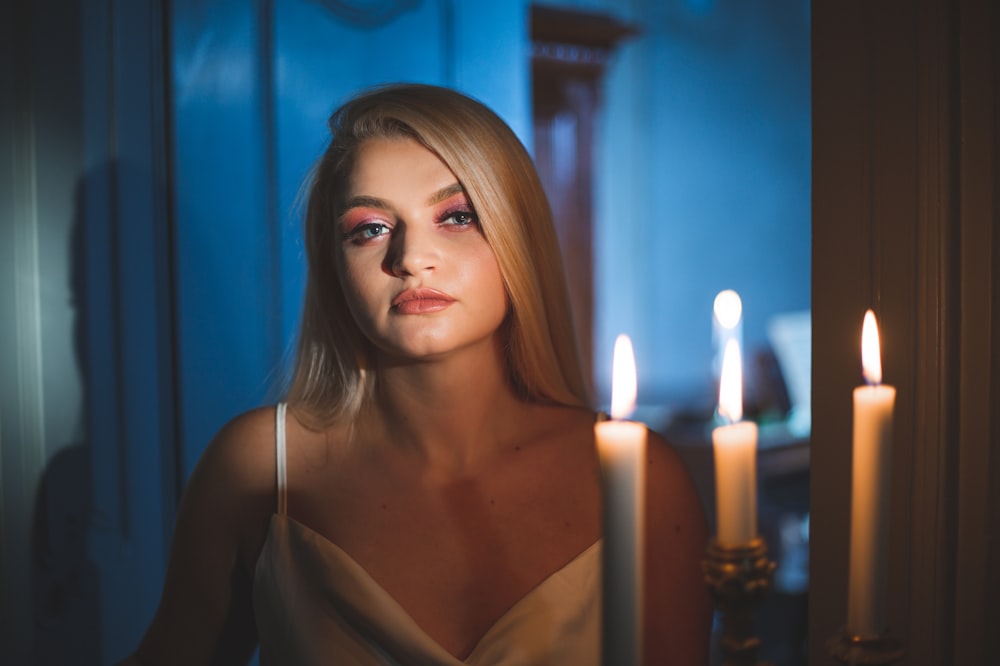 a woman with long blonde hair standing in front of a candle