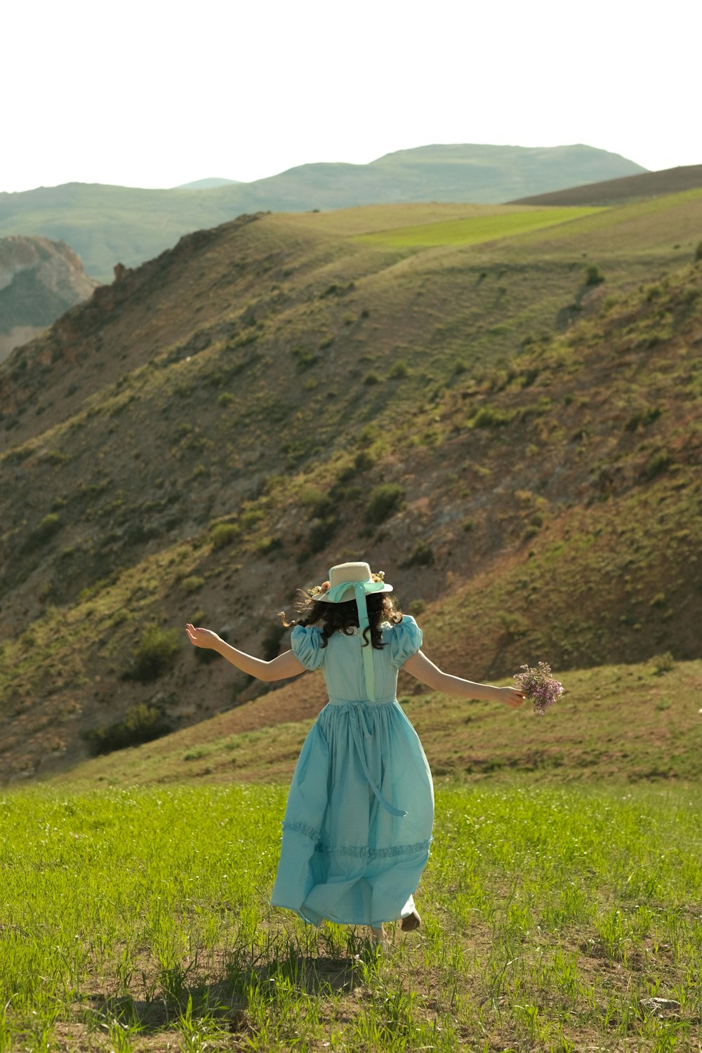 a woman in a blue dress and hat walking through a field