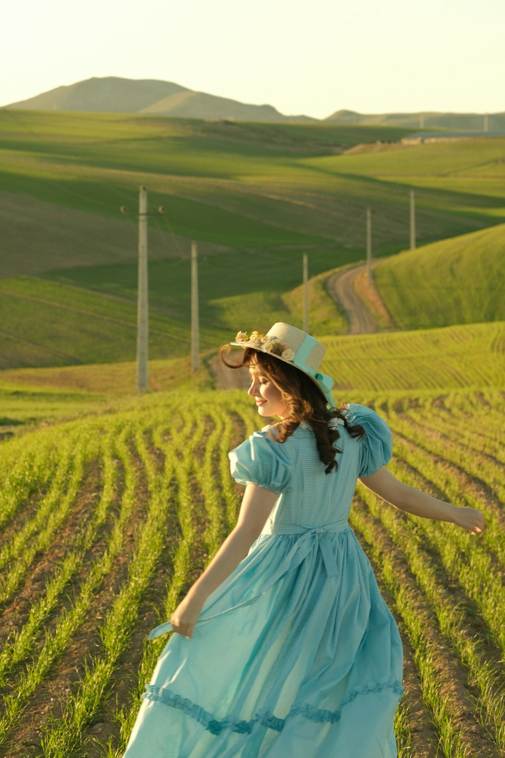 a woman in a blue dress and hat in a field