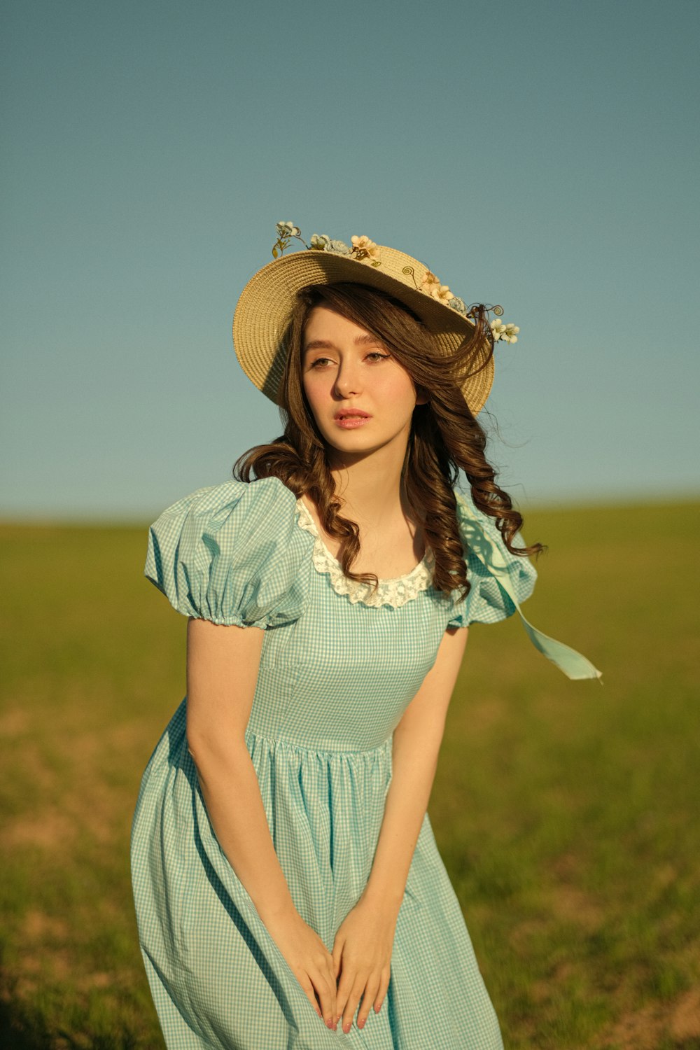 a woman in a dress and hat standing in a field