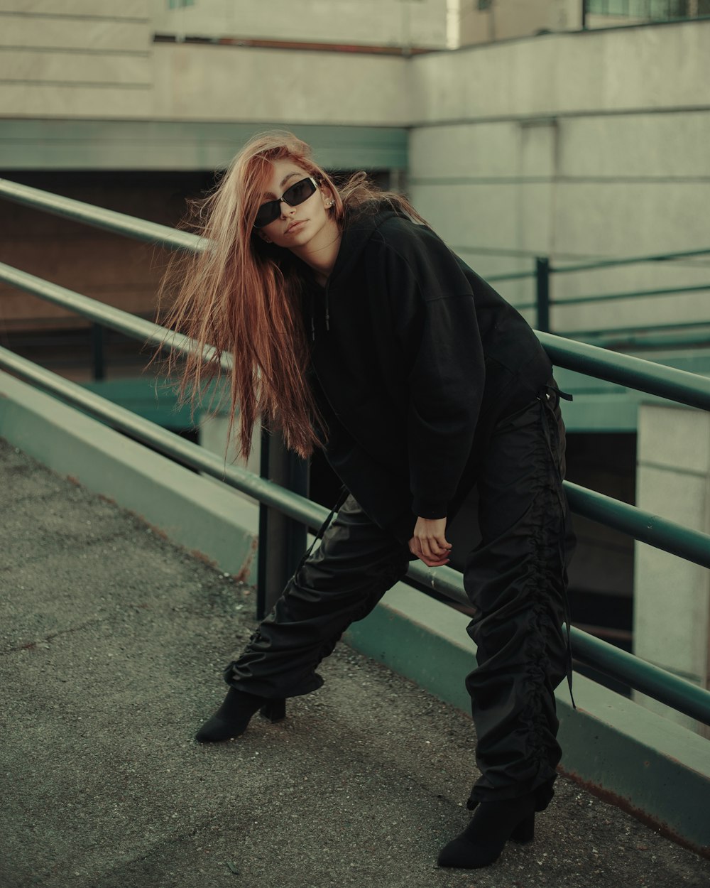 a woman with red hair and sunglasses leaning against a railing