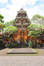 A vibrant Balinese temple gate surrounded by lush tropical greenery under a bright blue sky.