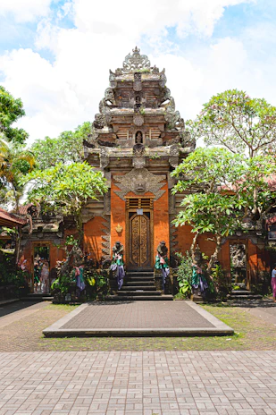 A vibrant Balinese temple gate surrounded by lush tropical greenery under a bright blue sky.