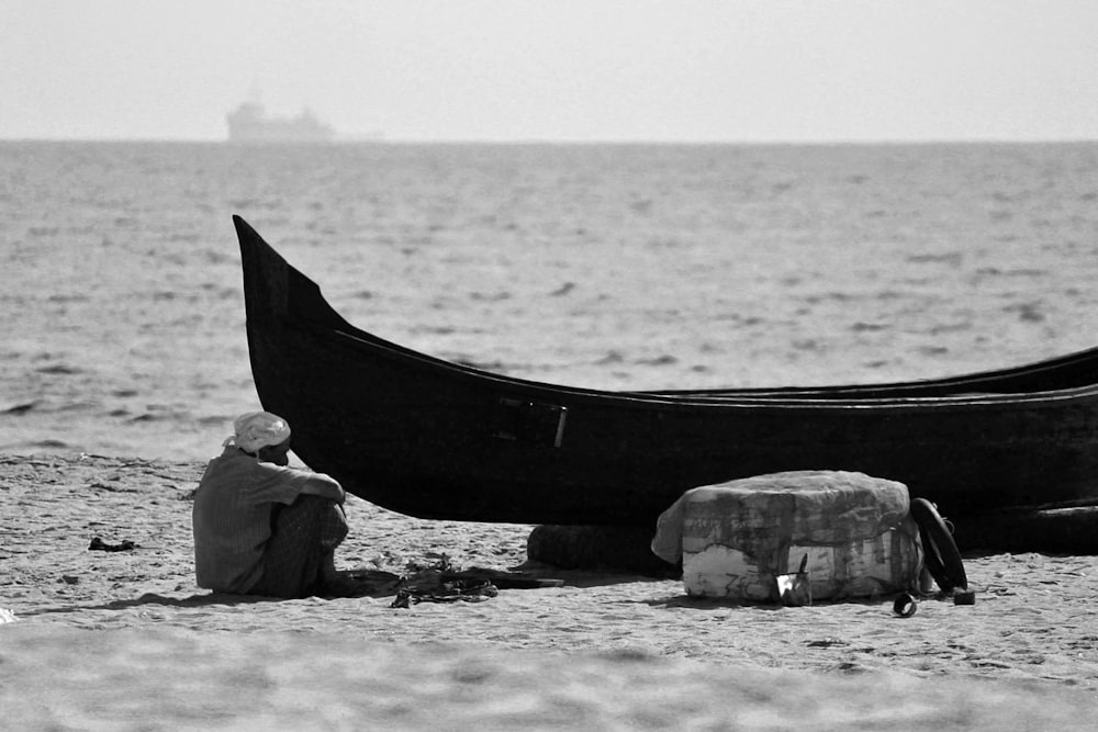a man sitting on the beach next to a boat