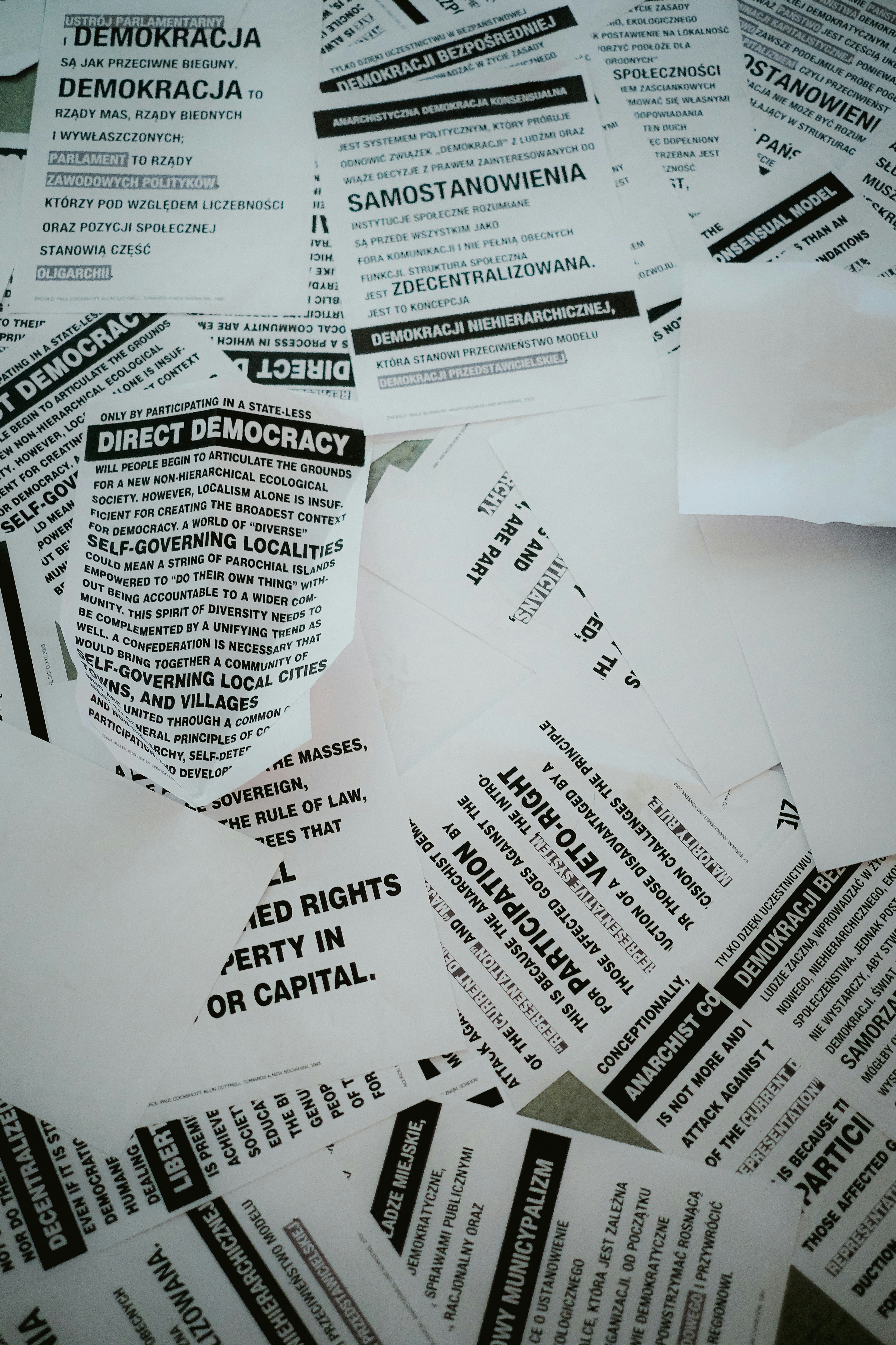 A collection of scattered flyers and papers with text related to concepts of democracy, rights, and anarchism. The papers are primarily in black and white and feature both English and Polish text.
