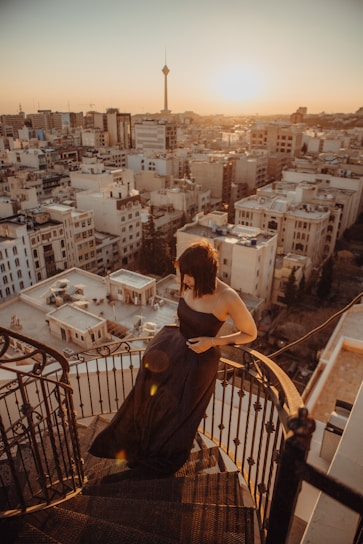 Elegant woman in a sleek black dress standing by a city skyline at dusk.