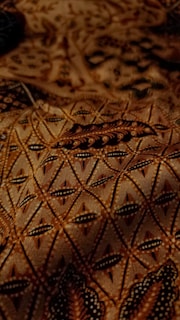 Elegant Arabian-inspired pattern in deep brown and gold hues, softly illuminated against a black backdrop.