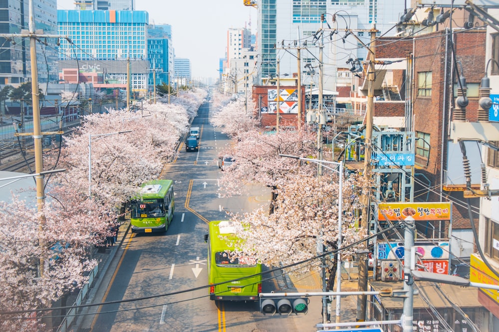 a couple of green trucks driving down a street next to tall buildings