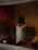 Several large bags filled with various items are stacked against a tiled wall. The bags are made of heavy fabric and are resting on top of plastic crates. There is a red poster with Chinese characters on the door to the left. A bucket is placed on the pavement in front of the bags.