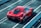 A sleek red sports car is parked on a racetrack with prominent aerodynamic design elements and a shiny finish. The car is viewed from the rear side, highlighting its detailed rear lights and large exhausts. Concrete barriers line the track, creating a controlled environment for high-speed testing.