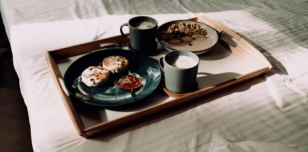 Smiling guest enjoying a breakfast tray by a sunlit window in a homely setting.
