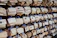 Wooden ema plaques hang densely on a structure, each displaying handwritten messages or prayers in various languages. Many of the plaques feature a printed design of a flower and cart, along with stamps or seals.