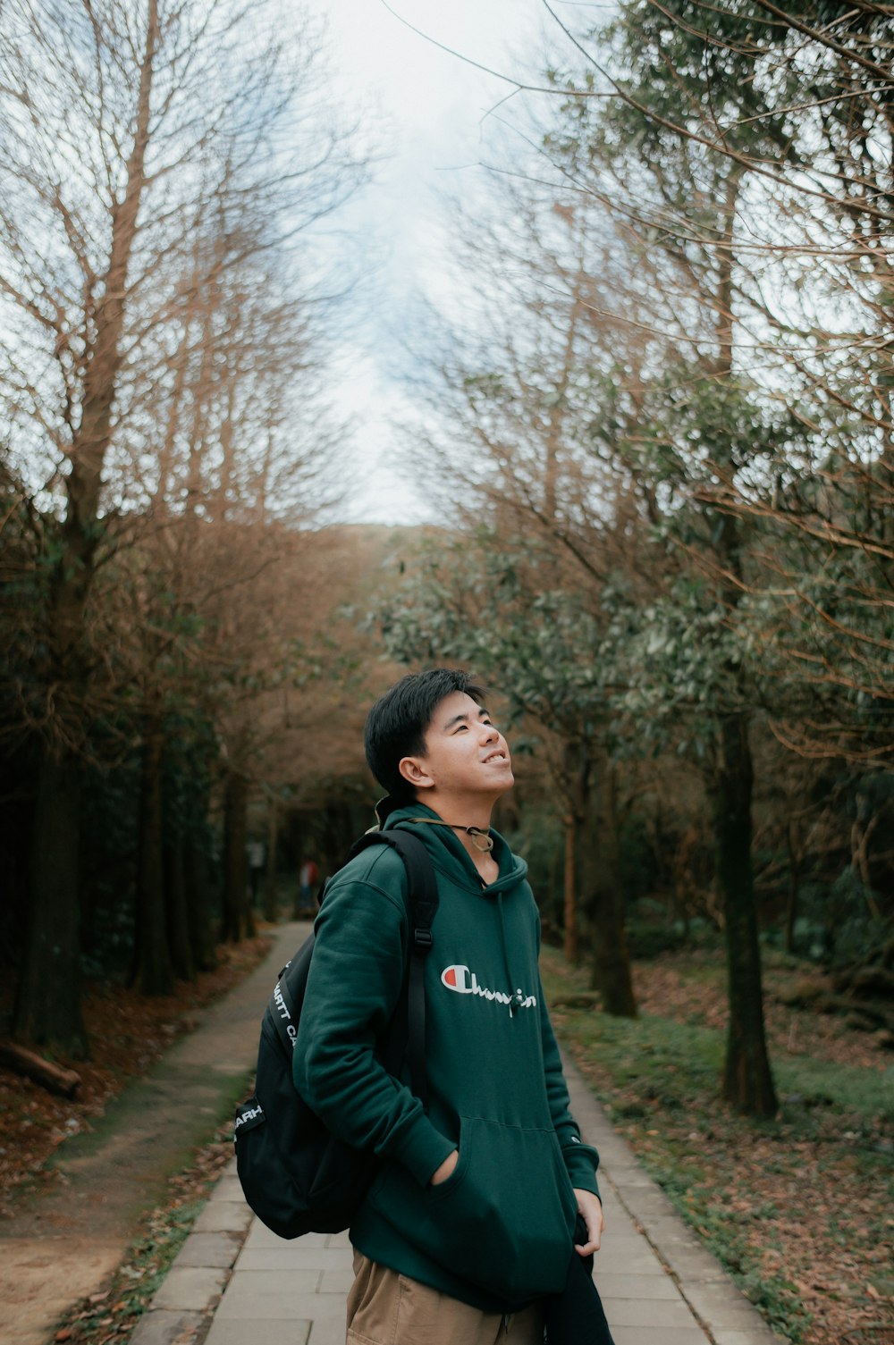 a young man standing on a sidewalk in a park